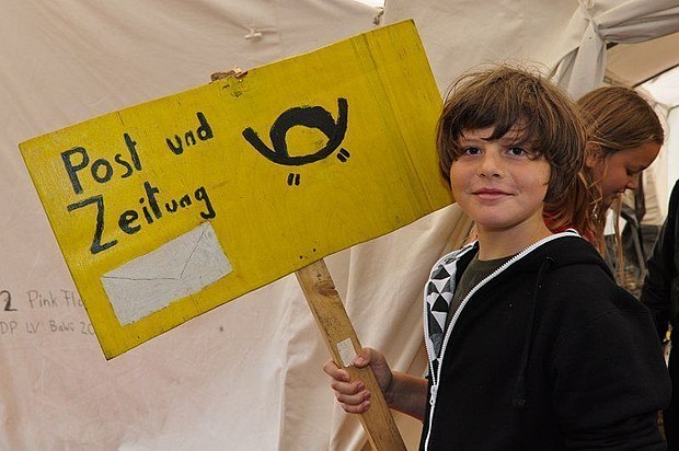 Kind auf einem Zeltlager, vor einem Zelt mit einem Schild in der Hand.